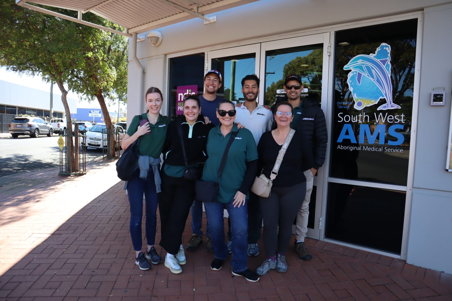 A group of seven people, including Johann, smiling while standing in front of the South West Aboriginal Medical Service building.